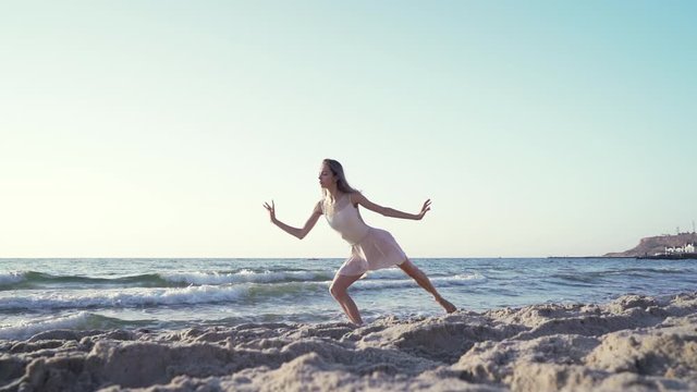 Slender beautiful ballerina in white dress dancing ballet on sea or ocean sandy beach in morning light. Concept of art, nature beauty