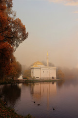 Fototapeta premium Russia, St. Petersburg, October 17, 2018, Catherine Park. In the photo, Turkish Bath in Tsarskoye Selo against the backdrop of an autumn park with red leaves and reflection in the lake in heavy fog