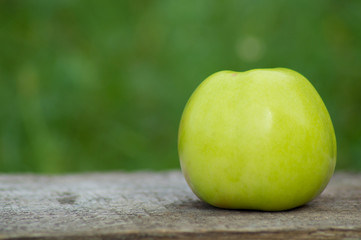 Large single green Apple on a wooden Board on a green background.Photo.Image of a beautiful fruit.Close up.Side view.natural fresh Apple.