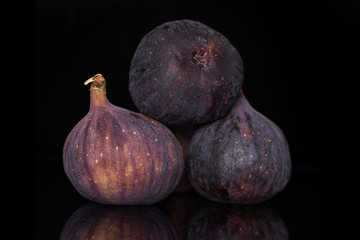 Group of three whole ripe fresh fig fruit isolated on black glass