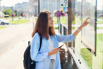Stylish girl looks to map of public transport to find the right station while standing at the modern tram station outdoors