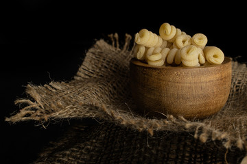 Lot of whole fresh raw pasta fusilli bucati in wooden bowl on jute cloth isolated on black glass
