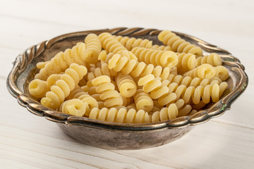 Lot of whole fresh raw pasta fusilli bucati in old iron bowl on white wood