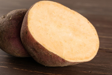 One half of fresh brown sweet potato on brown wood