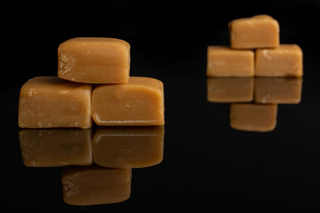 Group of six whole sweet golden caramel candy isolated on black glass