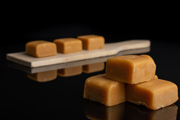 Lot of whole sweet golden caramel candy on small wooden cutting board isolated on black glass