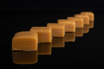 Group of seven whole sweet golden caramel candy isolated on black glass
