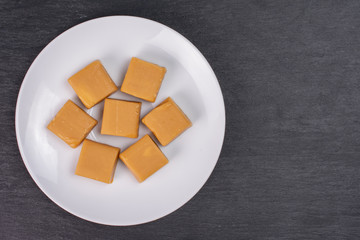 Group of seven whole sweet golden caramel candy on white ceramic plate flatlay on grey stone