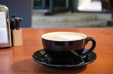 A black cup with a coffee saucer, a napkin stand, stands on a table of a street cafe terrace opposite the steps of the cafe entrance