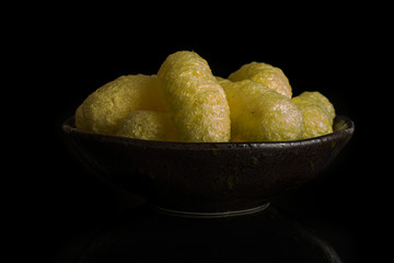 Lot of whole salted yellow corn puff in dark ceramic bowl isolated on black glass