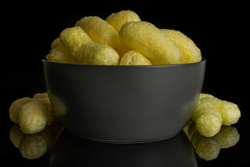 Lot of whole salted yellow corn puff in gray ceramic bowl isolated on black glass