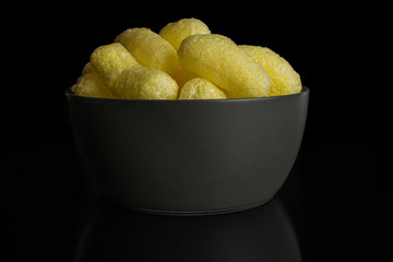Lot of whole salted yellow corn puff in gray ceramic bowl isolated on black glass