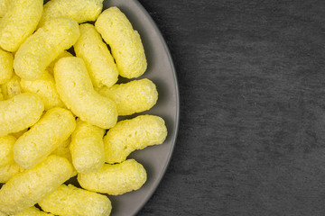 Lot of whole salted yellow corn puff on gray ceramic plate flatlay on grey stone
