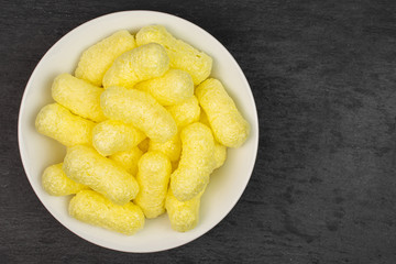 Lot of whole salted yellow corn puff on white ceramic plate flatlay on grey stone