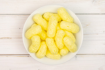 Lot of whole salted yellow corn puff on white ceramic plate flatlay on white wood