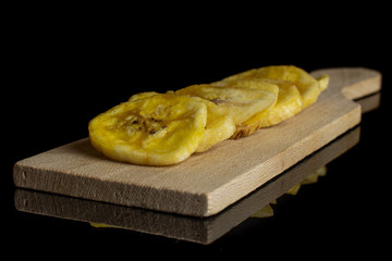Group of seven slices of sweet yellow dry banana on small wooden cutting board isolated on black glass
