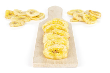 Lot of slices of sweet yellow dry banana on small wooden cutting board isolated on white background