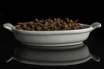 Lot of whole dry brown clove in white oval ceramic bowl isolated on black glass