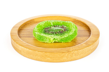 One slice of sweet green candied kiwifruit on bamboo coaster isolated on white background
