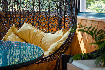 Room decor, cocoon chair with yellow pillows, glass table, plants and wooden wall