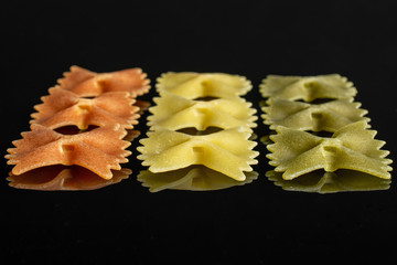 Group of nine whole red, yellow and green uncooked farfalle isolated on black glass