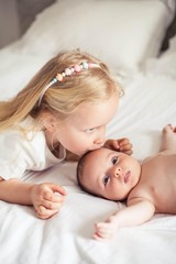 Young beautiful mother holds a baby. Little sister kisses her little sister. Baby. Children bedroom.