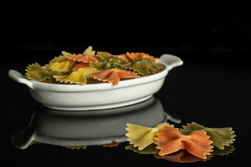 Lot of whole red, yellow and green uncooked farfalle three are in the front and the rest is isolated on black glass