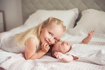 Young beautiful mother holds a baby. Little sister kisses her little sister. Baby. Children bedroom.