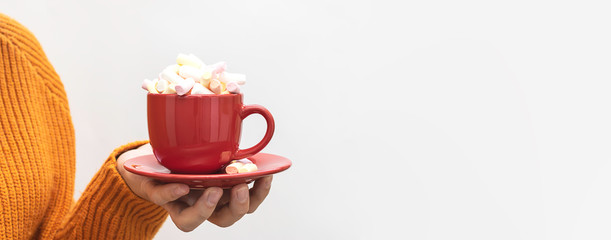 Long wide banner with woman in cozy warm sweater holding red cup of hot cacao drink with marshmallows, copy space for your text.
