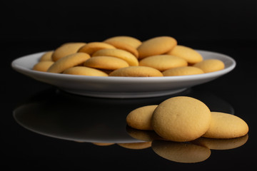 Lot of whole sweet golden sponge biscuit on white ceramic plate isolated on black glass