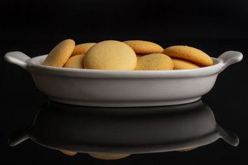 Lot of whole sweet golden sponge biscuit in white oval ceramic bowl isolated on black glass