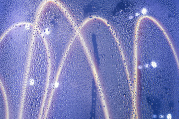  drops of water flow down the glass on a blue neon background. condensation on glass