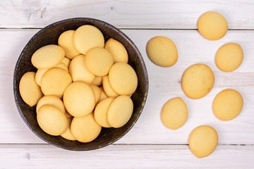 Lot of whole sweet golden sponge biscuit in dark ceramic bowl flatlay on white wood