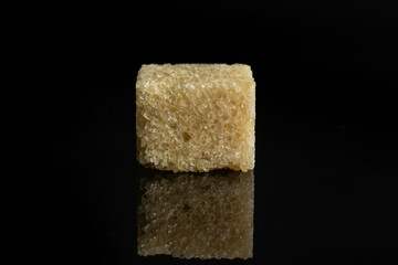 One whole sweet brown sugar cube isolated on black glass