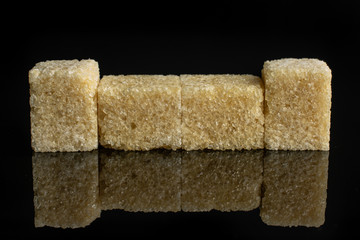 Group of four whole sweet brown sugar cube isolated on black glass