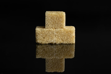 Group of three whole sweet brown sugar cube isolated on black glass