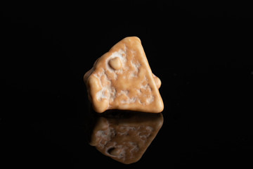 One whole beige sweet chocolate stone isolated on black glass