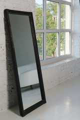 Black wooden rectangular vertical framed mirror beside big window