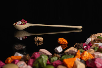 Lot of whole sweet chocolate stone in a wooden spoon isolated on black glass