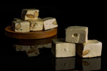 Lot of whole sweet white nougat on bamboo coaster isolated on black glass
