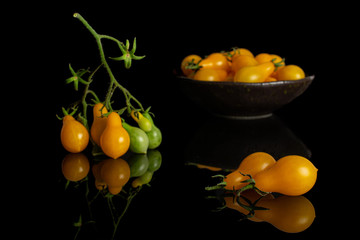 Lot of whole fresh yellow pear tomato in dark ceramic bowl isolated on black glass