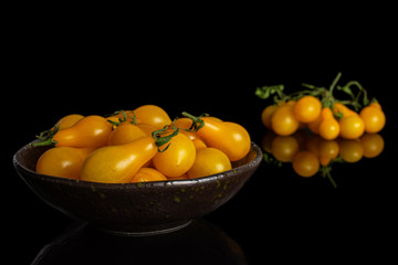 Lot of whole fresh yellow pear tomato in dark ceramic bowl isolated on black glass