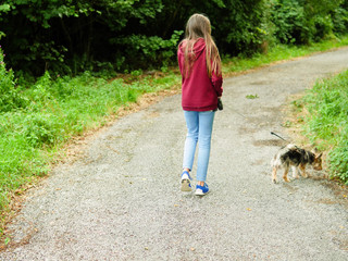 Girl walking her pet terrier in a park on a leash.