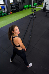Fototapeta na wymiar Young athletic woman exercising in gym using battle rope.
