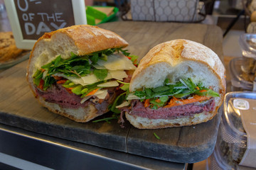 Closeup photo of a sandwich cut into three pieces on a white plate. Ingredients are slices of meat, arugula, sliced carrots and Swiss cheese. 