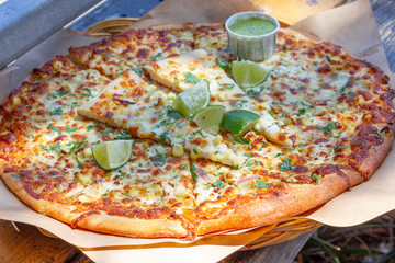 Artisan cheese pizza with corn, onion, pasilla peppers, mozzarella and Valbreso feta cheese, garlic olive oil, cilantro, and lime, with two sample slices on top and a small container of green sauce.