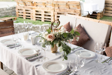 Wedding table setting decorated with fresh flowers in a brass vase. Wedding floristry. Banquet table for guests outdoors with a view of green nature. Bouquet with roses, eustoma and eucalyptus leaves