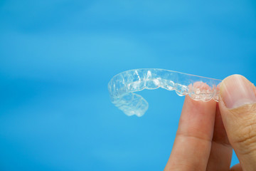 hand holding clear plastic retainer teeth that isolated on blue sky background. it's an equipment for orthodontist give the patient to orthodontic surgery in dental clinic or hospital
