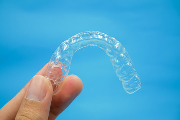 hand holding clear plastic retainer teeth that isolated on blue sky background. it's an equipment for orthodontist give the patient to orthodontic surgery in dental clinic or hospital