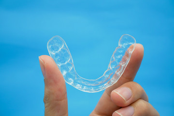 hand holding clear plastic retainer teeth that isolated on blue sky background. it's an equipment for orthodontist give the patient to orthodontic surgery in dental clinic or hospital